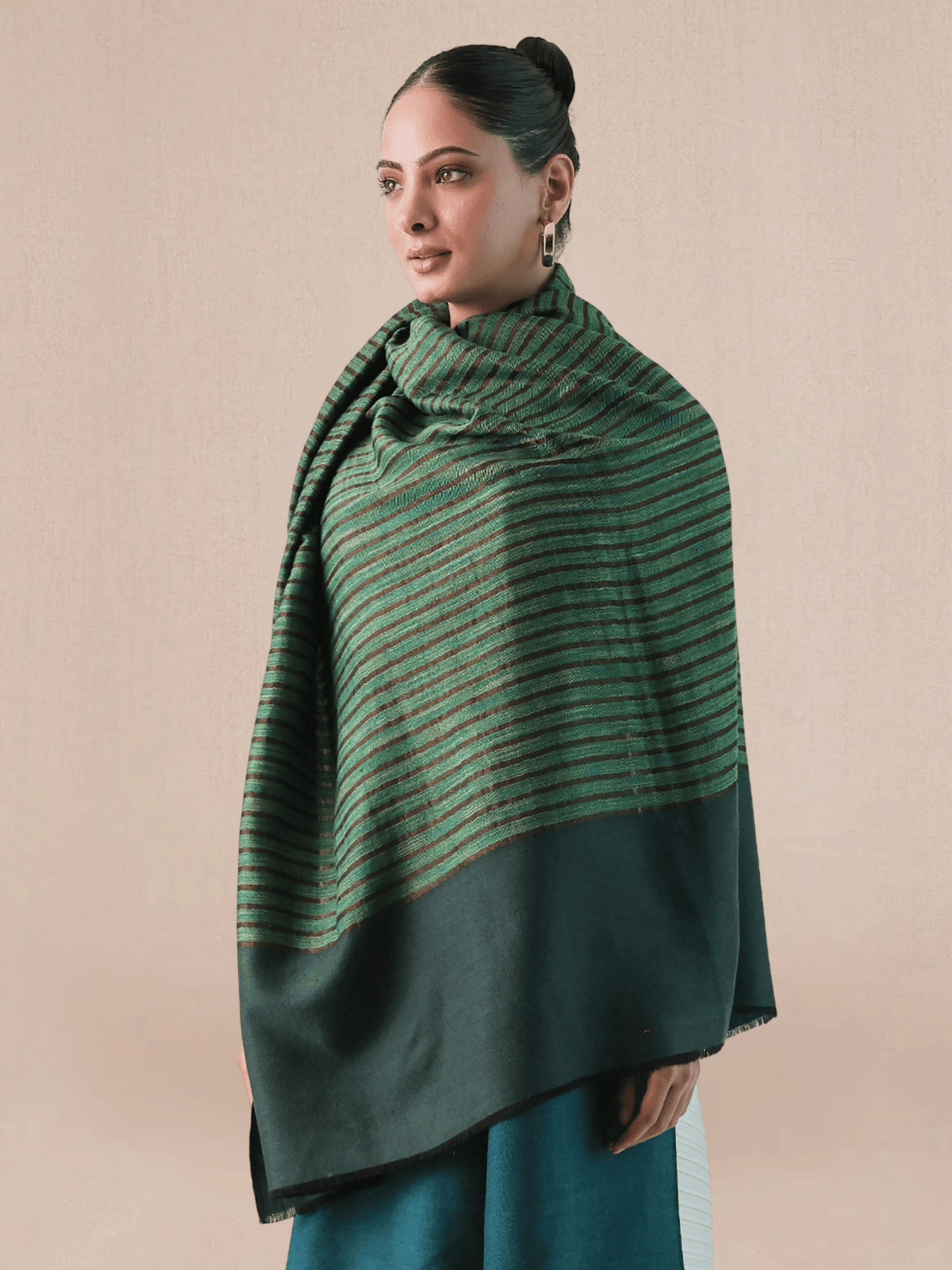 A woman wearing a pashmina shawl with a striped pattern in green, black, and teal colors, draped over the shoulders.