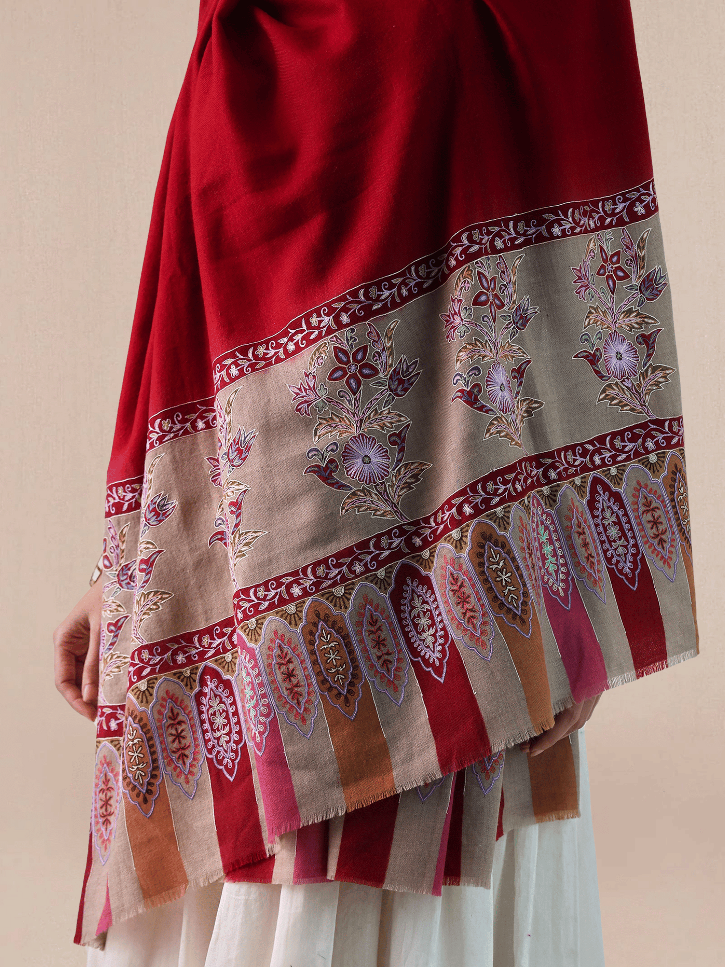 A woman wearing a vibrant red pashmina shawl with intricate floral embroidery and mehrabs.