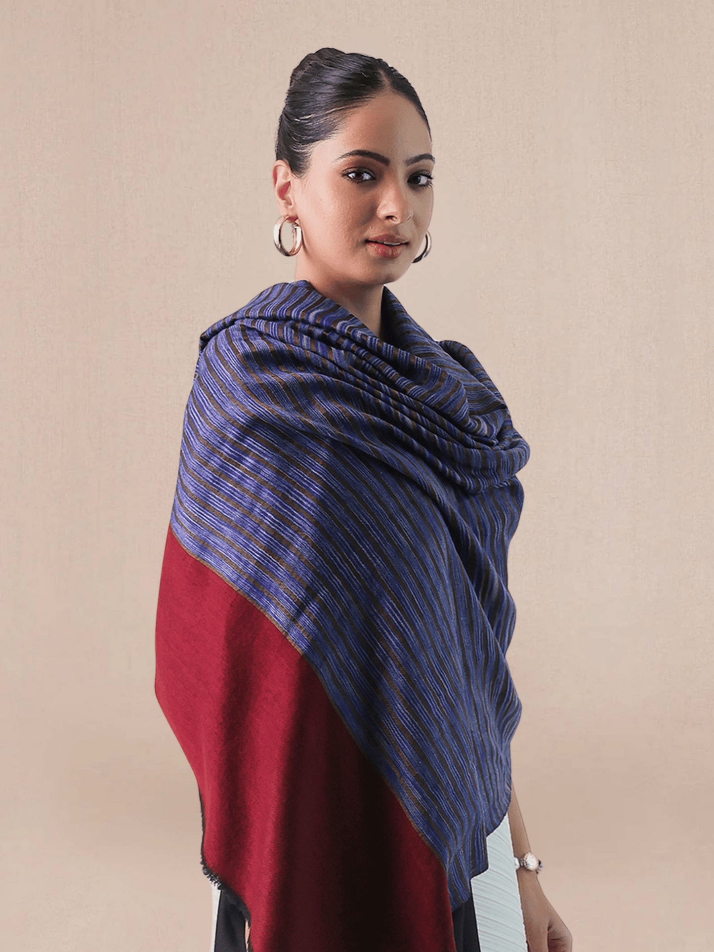 A woman wearing a pashmina shawl with a striped pattern in red and blue hues.