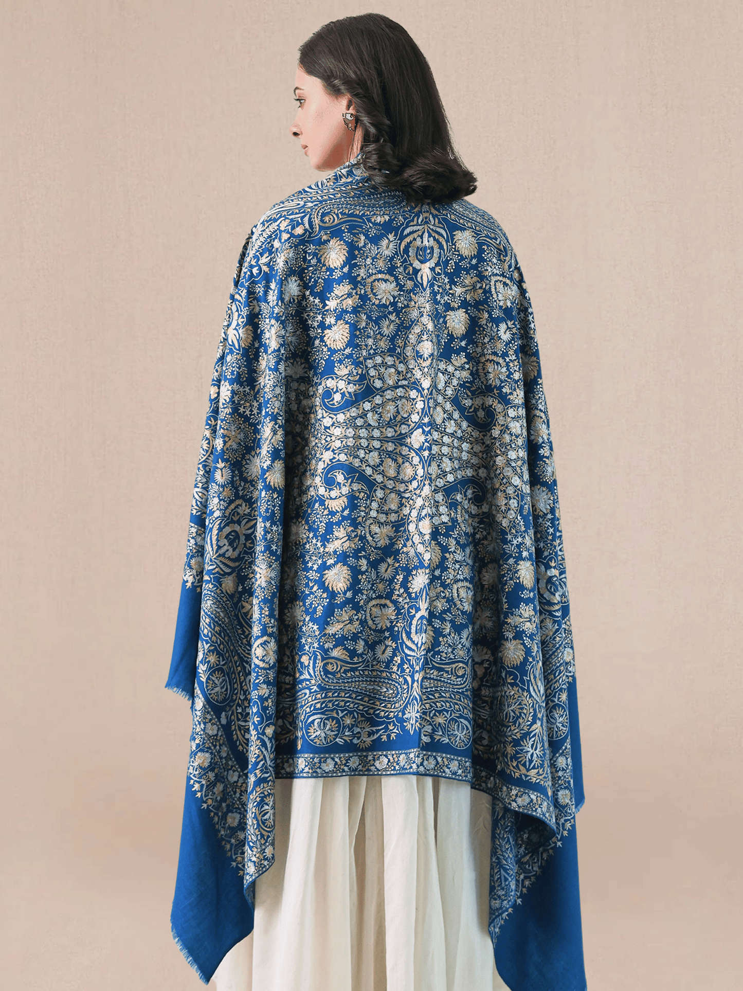 A woman wearing a royal blue pashmina shawl with intricate gold and silver zari embroidery in floral and paisley motifs, and a floral border.