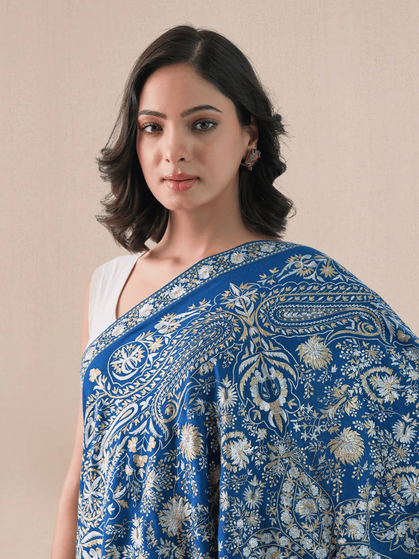 A woman wearing a royal blue pashmina shawl with intricate gold and silver zari embroidery in floral and paisley patterns.