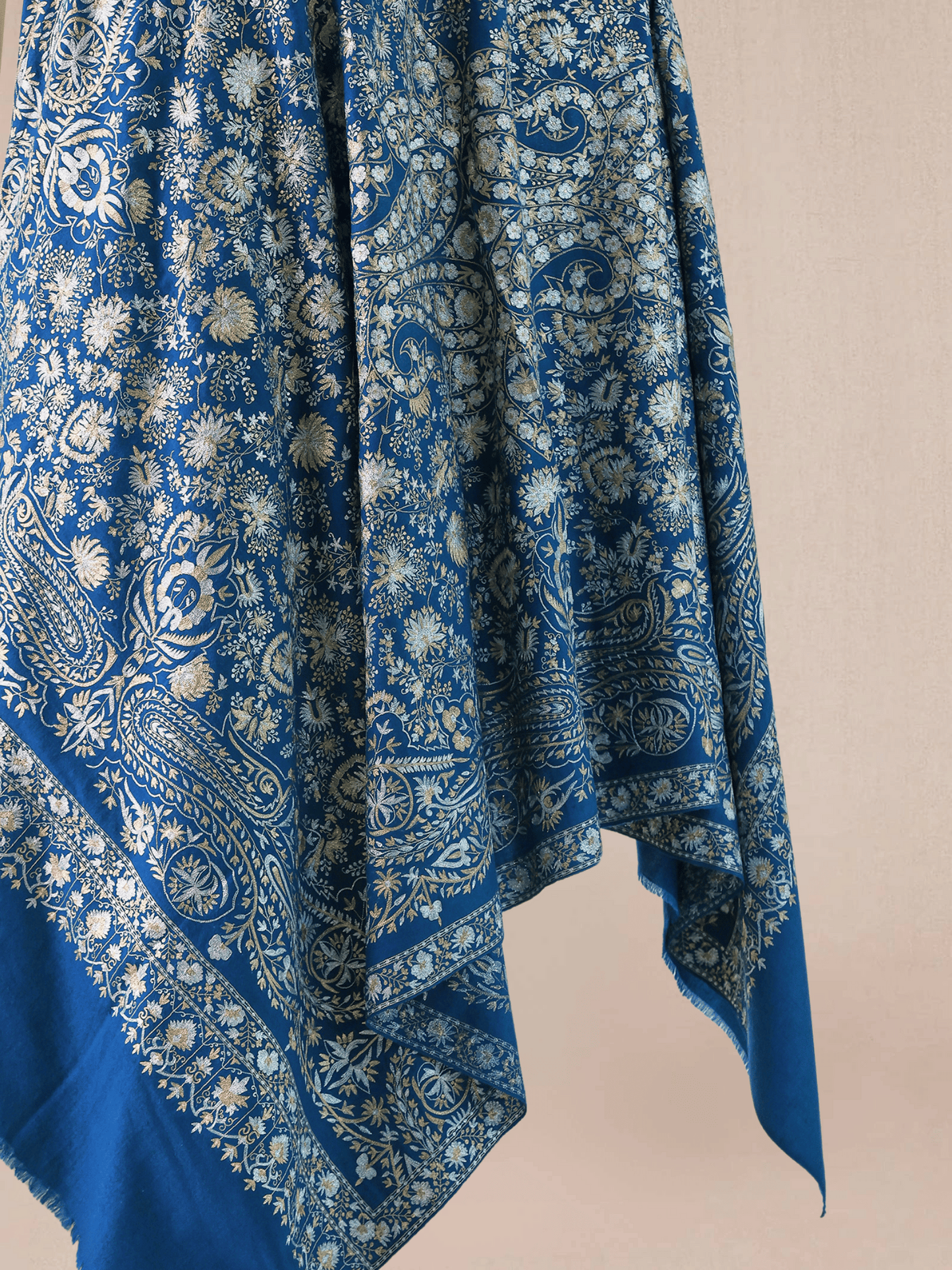 A woman wearing a royal blue pashmina shawl with intricate gold and silver zari embroidery in floral and paisley motifs, and a floral border.