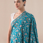 A woman wearing a bright blue pashmina shawl with gold and silver zari embroidery in floral and paisley motifs, and a floral border.