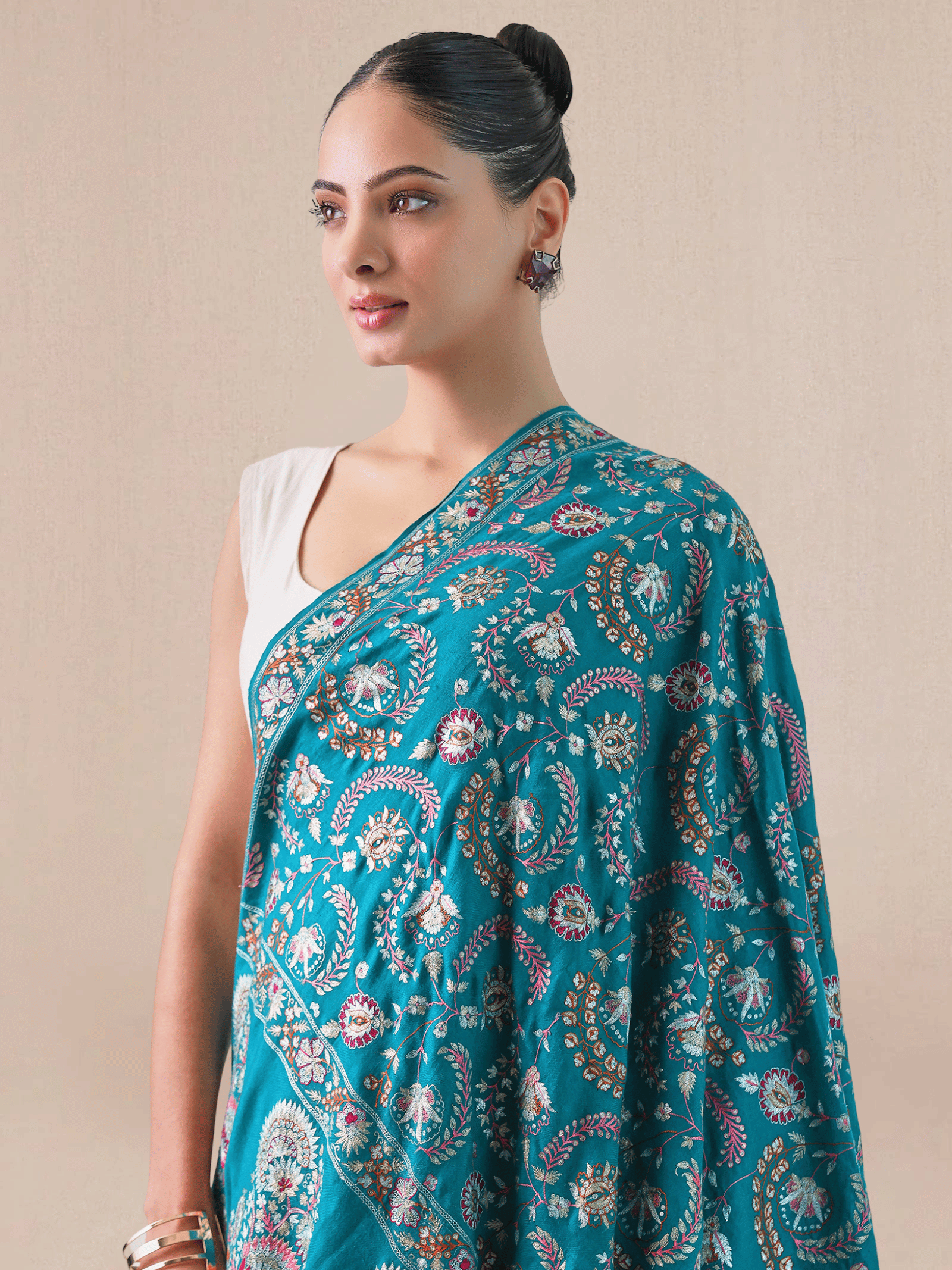 A woman wearing a bright blue pashmina shawl with gold and silver zari embroidery in floral and paisley motifs, and a floral border.