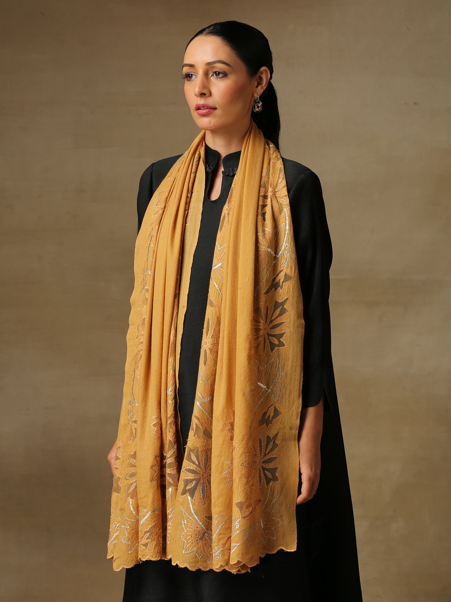 Model is wearing a Vineyard Zaywar stole featuring cutwork vine pattern bordered with zari details and hand embellished with fine swarovski, in a mustard colour.