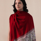 A woman wearing a vibrant red pashmina shawl with intricate floral embroidery and mehrabs.