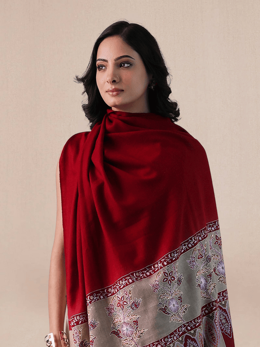 A woman wearing a vibrant red pashmina shawl with intricate floral embroidery and mehrabs.