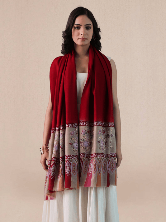 A woman wearing a vibrant red pashmina shawl with intricate floral embroidery and mehrabs.