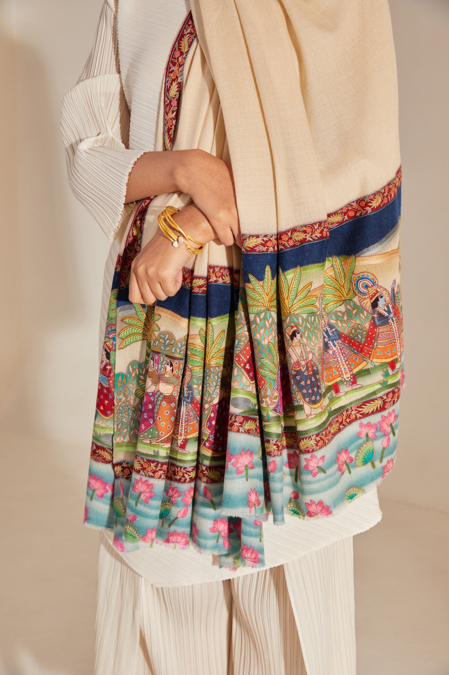 Model is wearing the Krishna Baraat Pashmina Shawl hand painted and hand embroidered on handloomed pashmina, depicting the secret wedding of Radha and Krishna, presided over by Lord Brahma. 