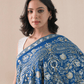 A woman wearing a royal blue pashmina shawl with intricate gold and silver zari embroidery in floral and paisley patterns.