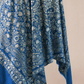 A woman wearing a royal blue pashmina shawl with intricate gold and silver zari embroidery in floral and paisley motifs, and a floral border.