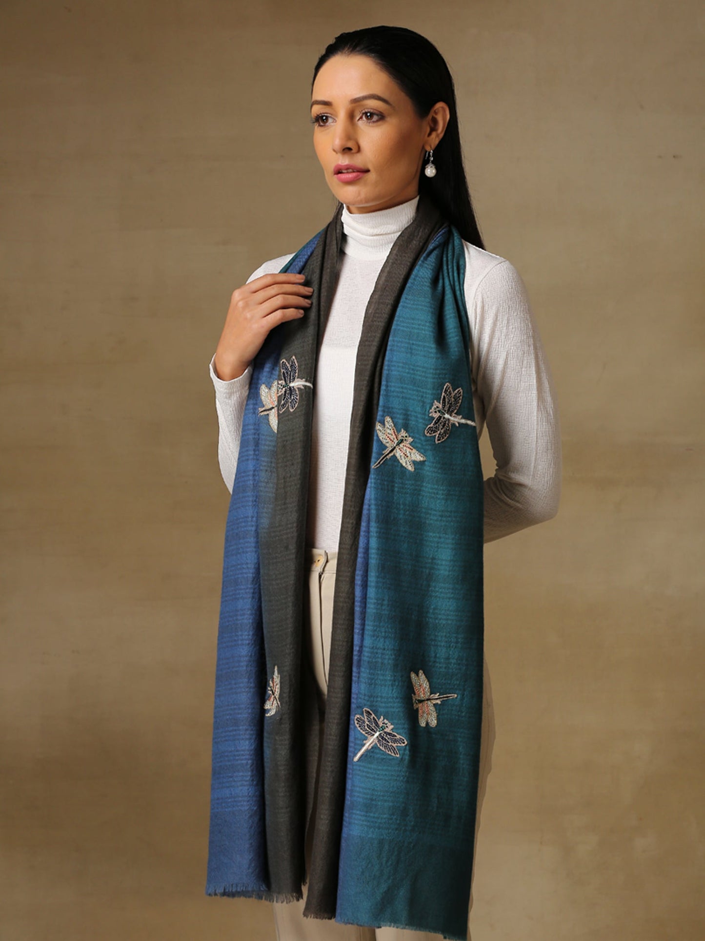 Model is wearing a Dragonfly stole in self weave handloomed pashmina featuring dragonflies hand embroidered using threadwork, pearls, cutdana and shellwork, on a handloomed ocean blue ombre pashmina. 