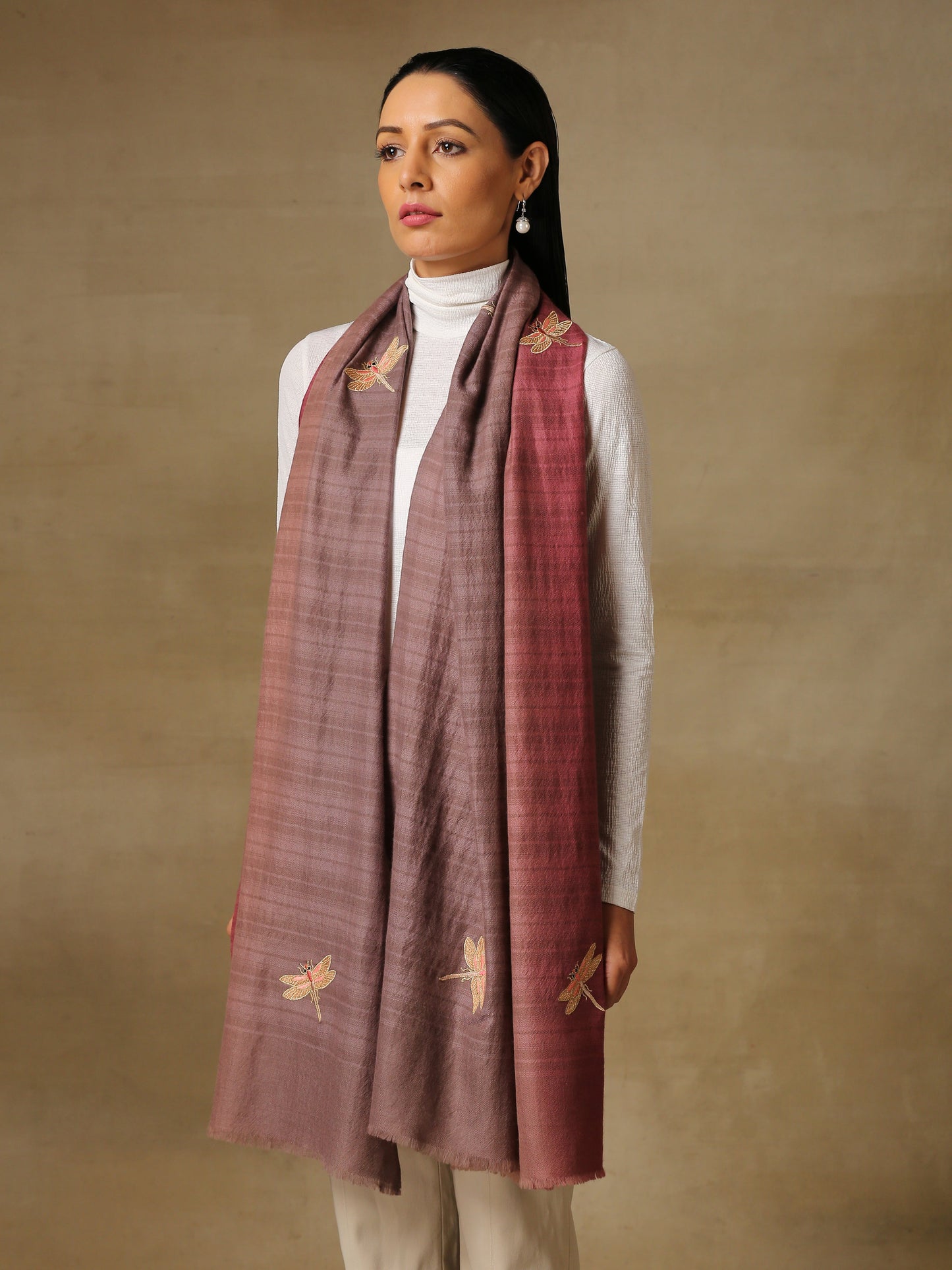 Model is wearing a Dragonfly stole in self weave handloomed pashmina featuring dragonflies hand embroidered using threadwork, pearls, cutdana and shellwork, on a handloomed  mauve and graypashmina. 