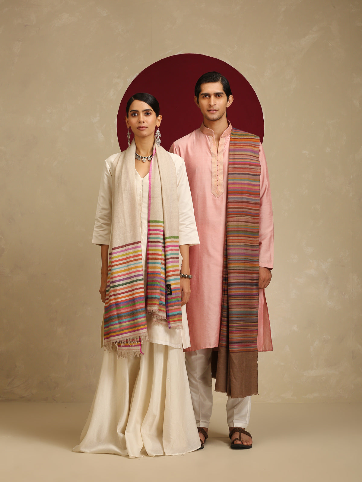 The model on the left is wearing a Pashmina Striped stole from shaza in a multicoloured stripes pattern on a white base. 