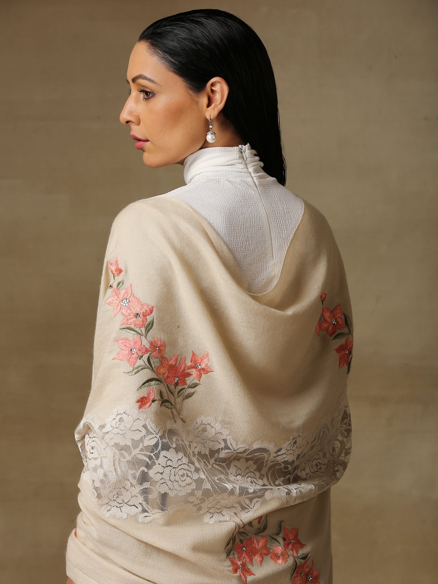 Model is wearing a Summer tales pashmina stole featuring flower motifs adorned with rhinestones and swarovski on a cream handloomed pashmina stole.