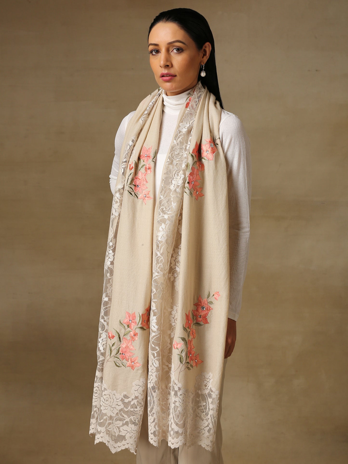 Model is wearing a Summer tales pashmina stole featuring flower motifs adorned with rhinestones and swarovski on a cream handloomed pashmina stole.