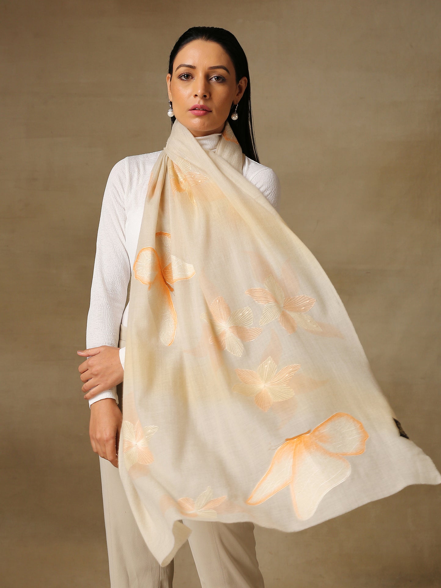 Model is wearing the butterfly pashmina stole from Shaza, featuring hand embroidered butterfly shapes decorated with swarovski on a cream pashmina stole. 