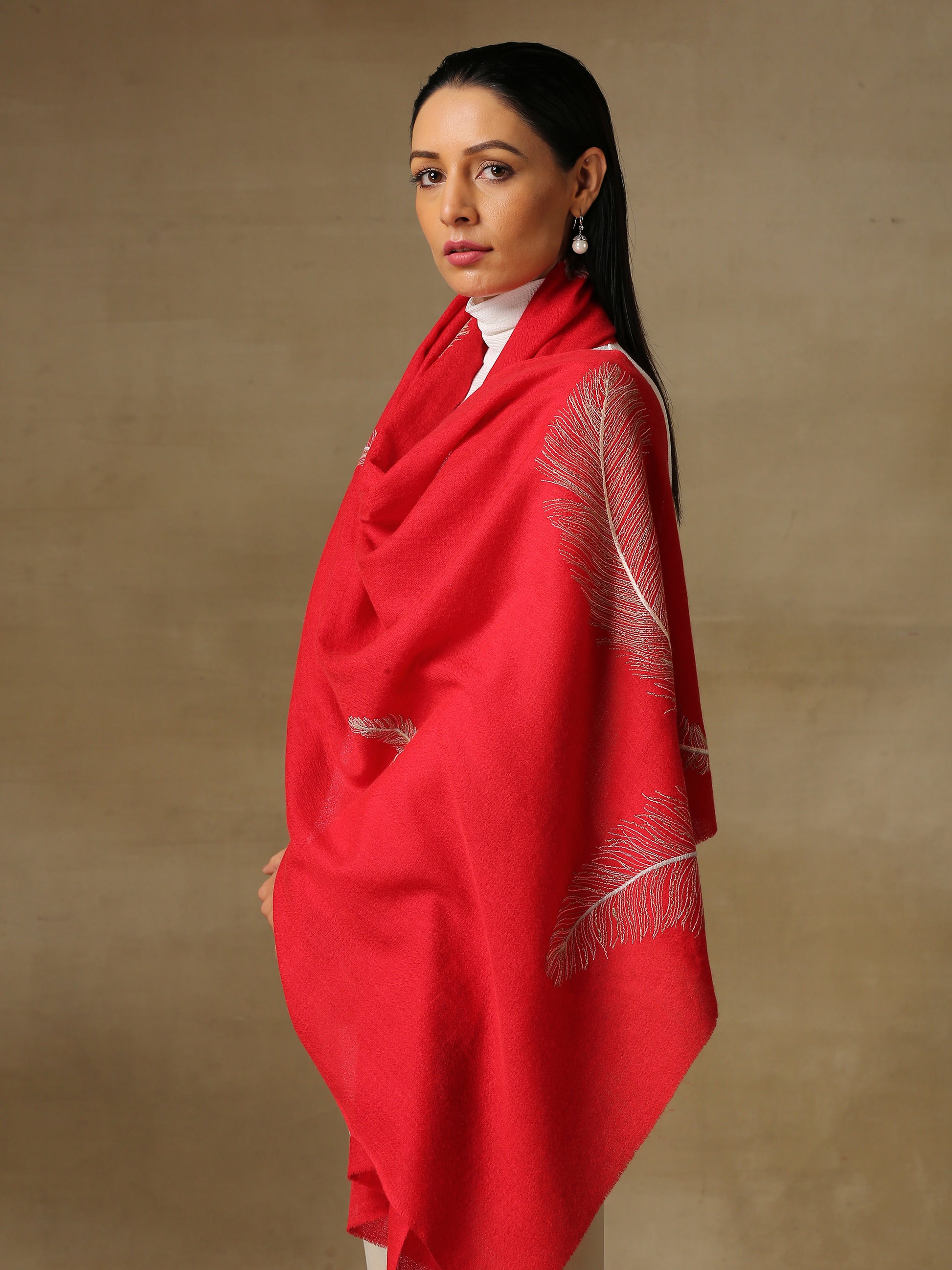 Model is wearing the Feather pashmina stole in the color red, featuring feather shapes hand embroidered using threadwork and zari. 
