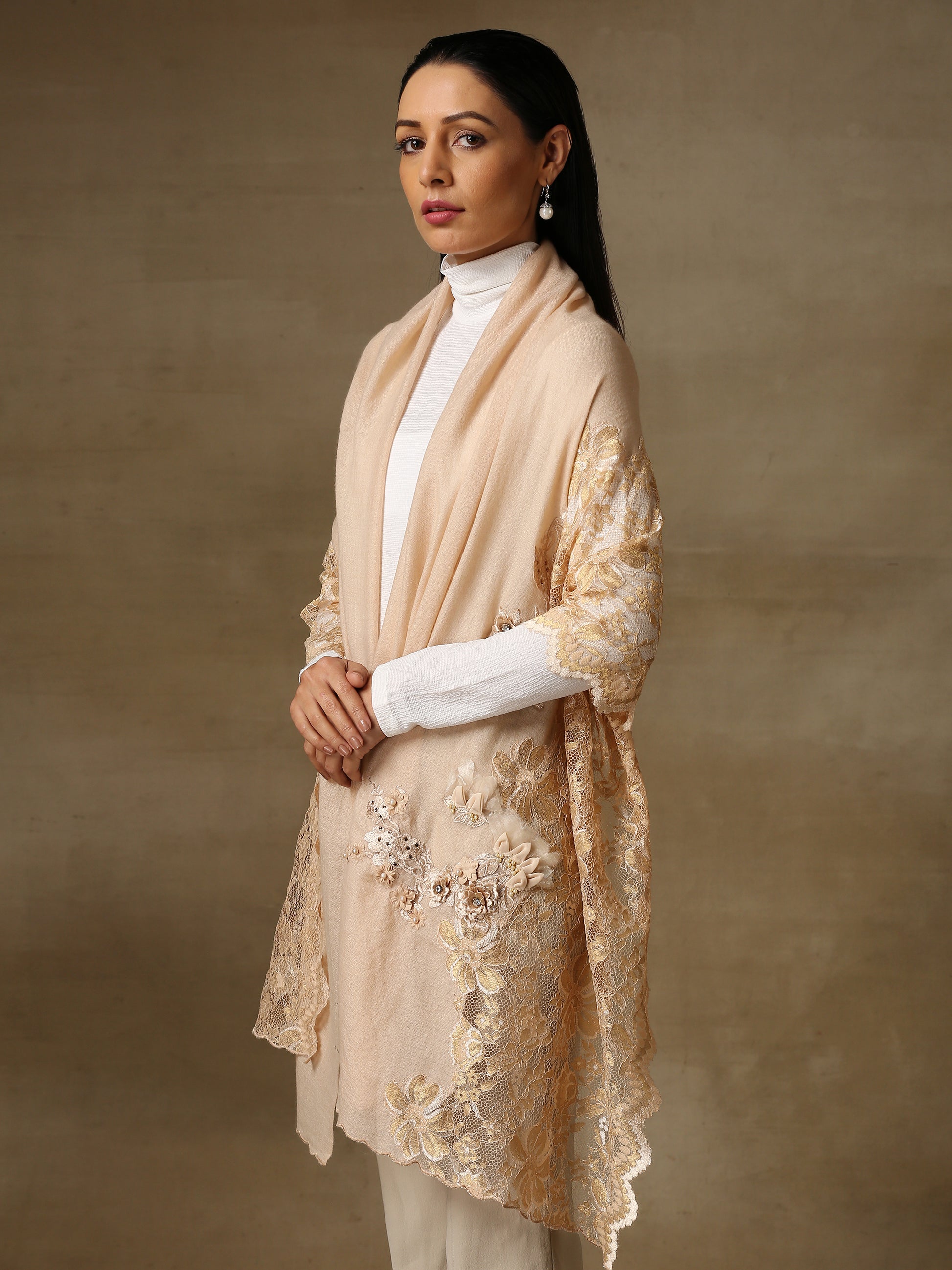 Model is wearing a pashmina stole in a peachy nude are lavishly embellished with floral motifs, made with threadwork, swarovski, pearls, and applique. This stole is from the Elements of spring collection.  