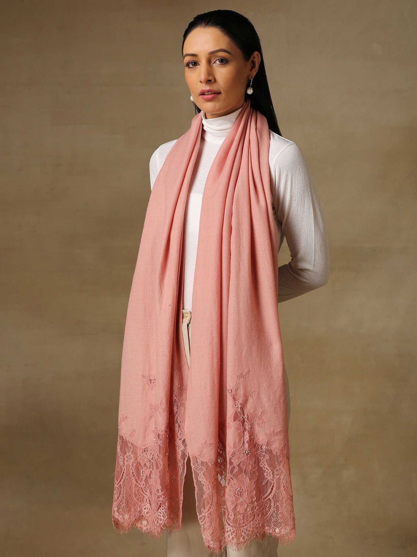 Model is wearing a pashmina stole in a peachy pink, lavishly embellished with floral motifs, made with threadwork, swarovski, pearls, and applique. This stole is from the Elements of spring collection.