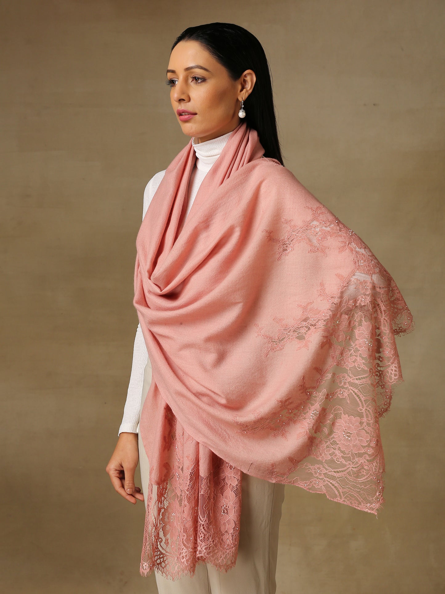 Model is wearing a pashmina stole in a peachy pink, lavishly embellished with floral motifs, made with threadwork, swarovski, pearls, and applique. This stole is from the Elements of spring collection.