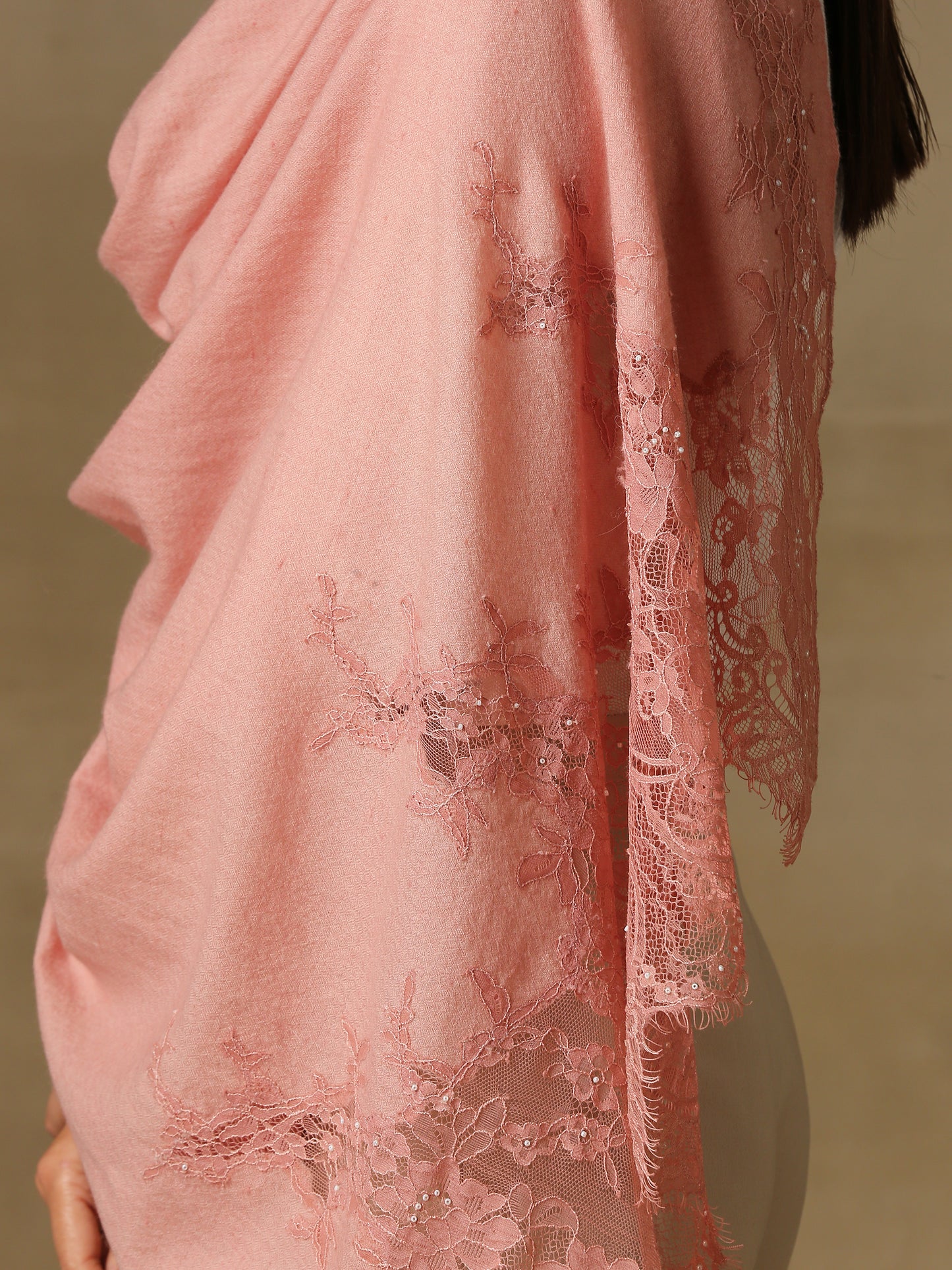 Model is wearing a pashmina stole in a peachy pink, lavishly embellished with floral motifs, made with threadwork, swarovski, pearls, and applique. This stole is from the Elements of spring collection.